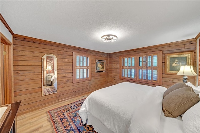 bedroom featuring hardwood / wood-style flooring, wooden walls, and a textured ceiling