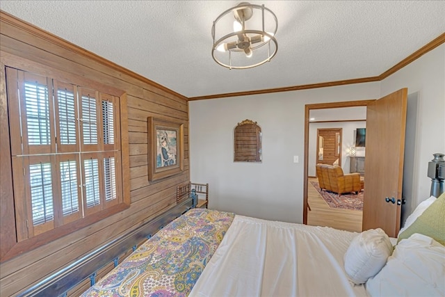 bedroom featuring a notable chandelier, wooden walls, ornamental molding, and a textured ceiling