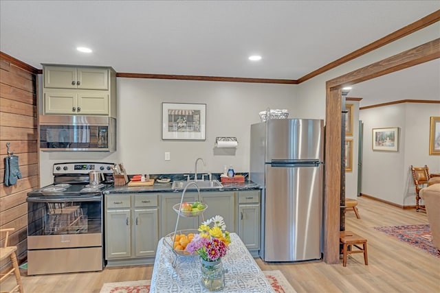 kitchen with appliances with stainless steel finishes, sink, dark stone counters, ornamental molding, and light hardwood / wood-style floors