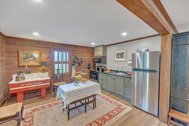 kitchen with stainless steel appliances, wooden walls, sink, ornamental molding, and light wood-type flooring