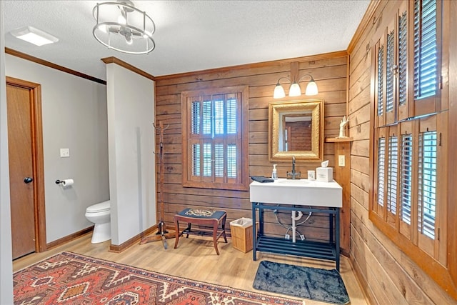 bathroom with a textured ceiling, wooden walls, toilet, hardwood / wood-style flooring, and crown molding