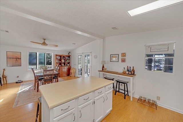 kitchen featuring white cabinets, a kitchen island, french doors, light wood-type flooring, and lofted ceiling with beams