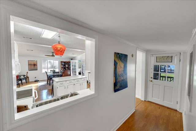 corridor with light hardwood / wood-style floors, a textured ceiling, lofted ceiling, and ornamental molding