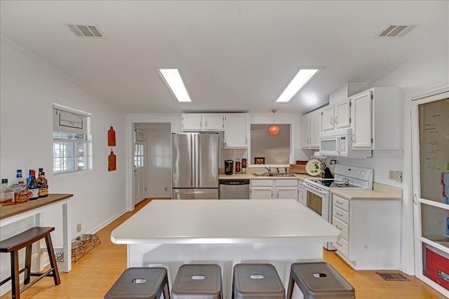 kitchen featuring pendant lighting, appliances with stainless steel finishes, white cabinetry, a kitchen breakfast bar, and sink