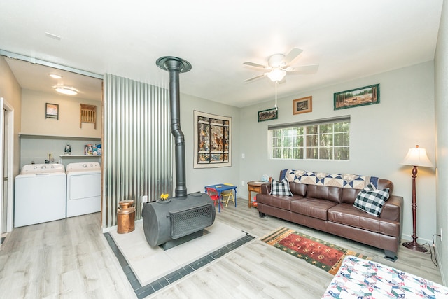 living room featuring washing machine and clothes dryer, light hardwood / wood-style floors, ceiling fan, and a wood stove