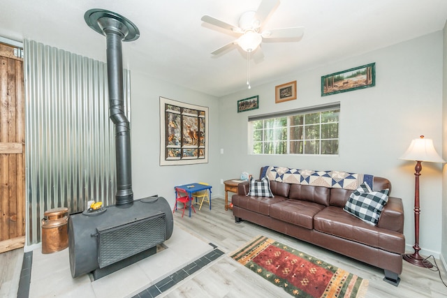 living room featuring ceiling fan, a wood stove, and light hardwood / wood-style flooring