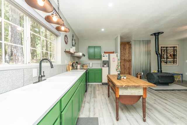 kitchen featuring sink, a wood stove, light hardwood / wood-style flooring, white refrigerator with ice dispenser, and green cabinetry