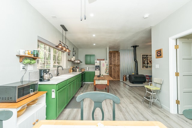 kitchen with sink, white refrigerator with ice dispenser, light hardwood / wood-style floors, decorative light fixtures, and green cabinetry