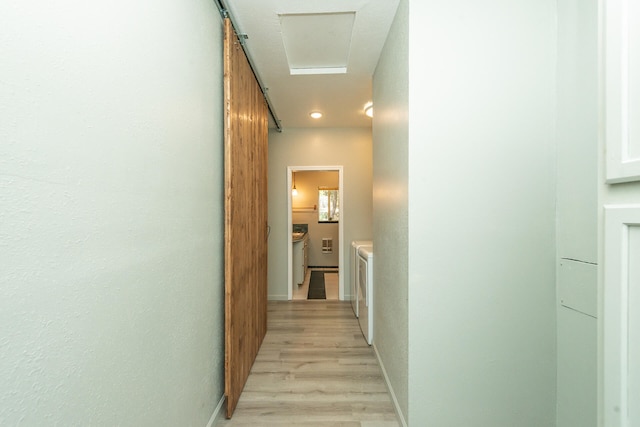 corridor featuring light hardwood / wood-style flooring, washing machine and clothes dryer, and a barn door