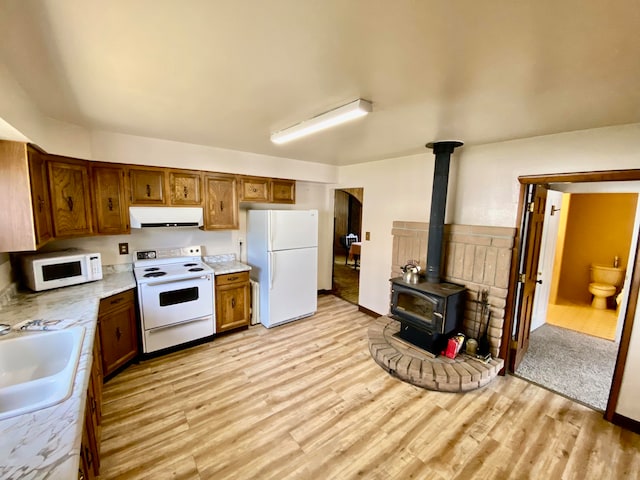 kitchen with sink, a wood stove, light wood-type flooring, and white appliances