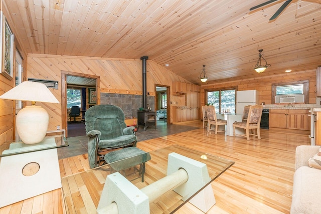 living room featuring light hardwood / wood-style flooring, a wood stove, wood walls, wooden ceiling, and ceiling fan