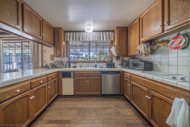 kitchen featuring sink, stainless steel dishwasher, backsplash, tile countertops, and dark wood-type flooring