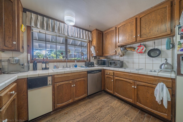 kitchen featuring sink, hardwood / wood-style floors, appliances with stainless steel finishes, backsplash, and tile countertops