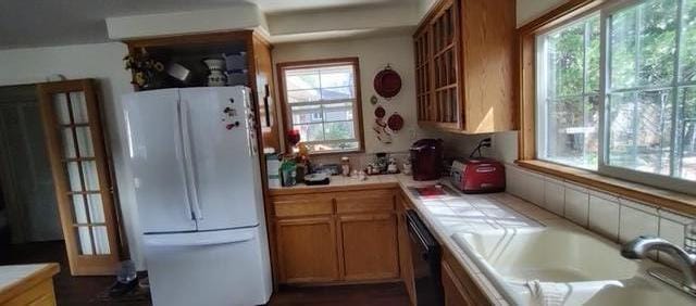 kitchen featuring plenty of natural light, tile counters, white fridge, and dishwasher