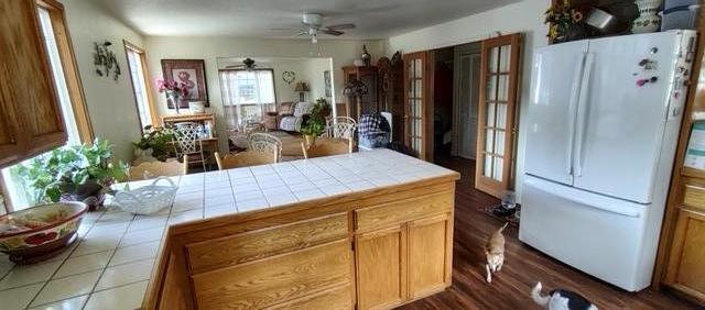 kitchen with ceiling fan, white fridge, tile counters, and wood-type flooring