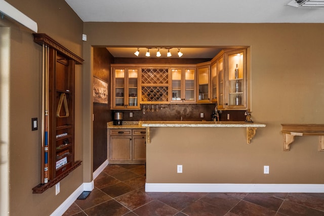 bar with dark tile flooring, rail lighting, tasteful backsplash, and light stone countertops