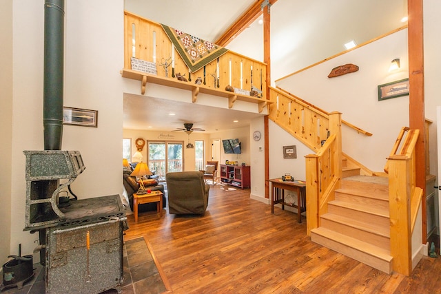 living room featuring a towering ceiling, dark hardwood / wood-style floors, ceiling fan, and a wood stove