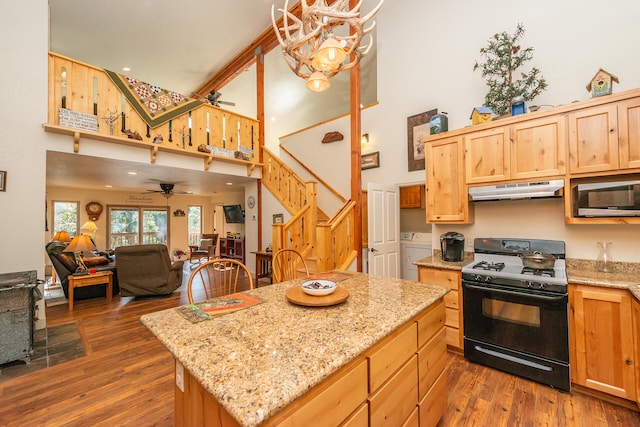 kitchen with gas stove, a towering ceiling, ceiling fan with notable chandelier, and dark hardwood / wood-style flooring