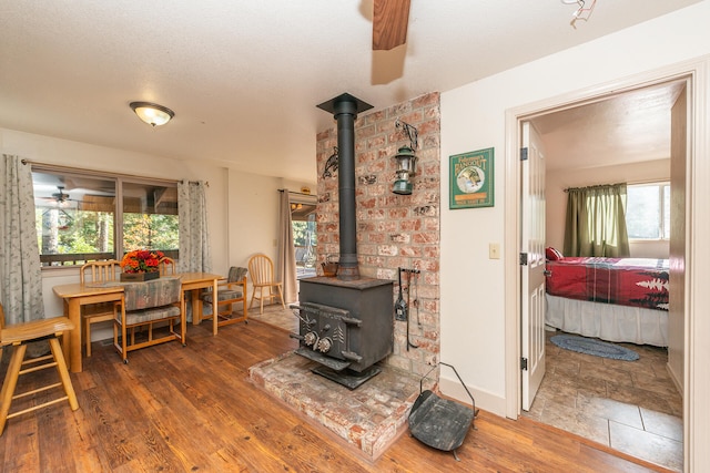 tiled living room with brick wall, ceiling fan, a wood stove, and a wealth of natural light