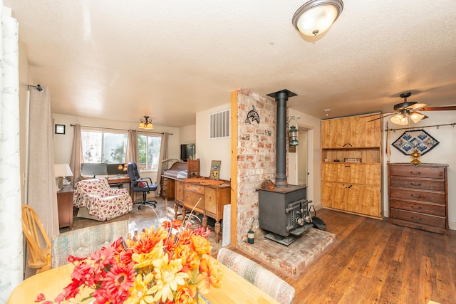 living room featuring dark wood-type flooring, a textured ceiling, ceiling fan, and a wood stove