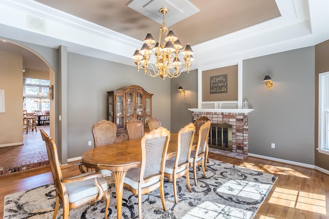 dining space featuring a notable chandelier, a fireplace, a tray ceiling, and wood-type flooring