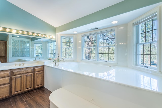 bathroom with plenty of natural light, large vanity, vaulted ceiling, and a bathing tub