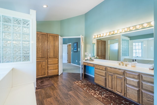 bathroom featuring hardwood / wood-style flooring, vaulted ceiling, a bath, and vanity