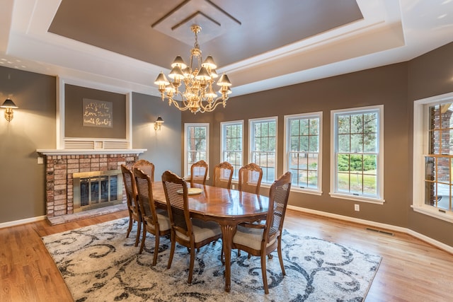 dining room with a tray ceiling, a brick fireplace, a notable chandelier, and light wood-type flooring