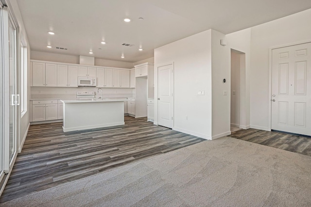 kitchen featuring white cabinets, range, an island with sink, and dark colored carpet