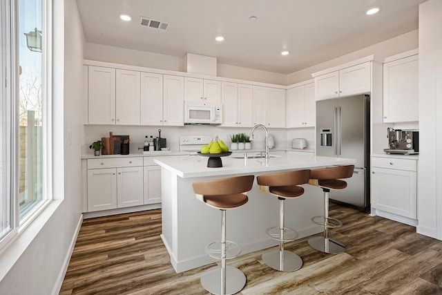 kitchen featuring dark hardwood / wood-style floors, white cabinets, white appliances, and a center island with sink