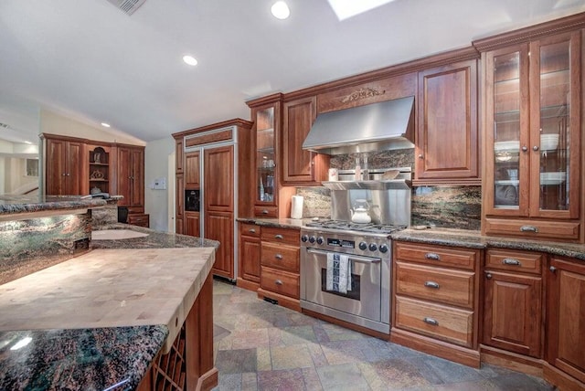 kitchen featuring lofted ceiling, high end range, tasteful backsplash, dark tile flooring, and wall chimney exhaust hood