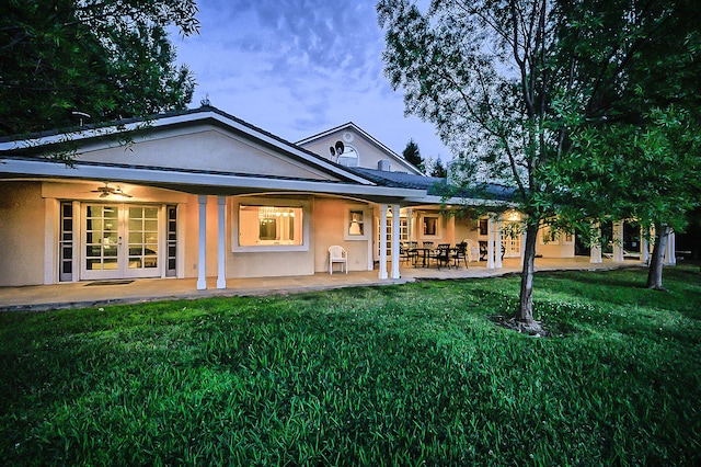 back house at dusk featuring a lawn and french doors