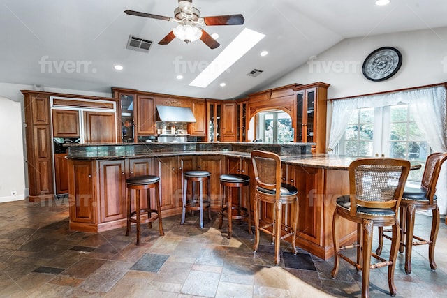 bar featuring range hood, dark stone countertops, vaulted ceiling with skylight, ceiling fan, and dark tile flooring