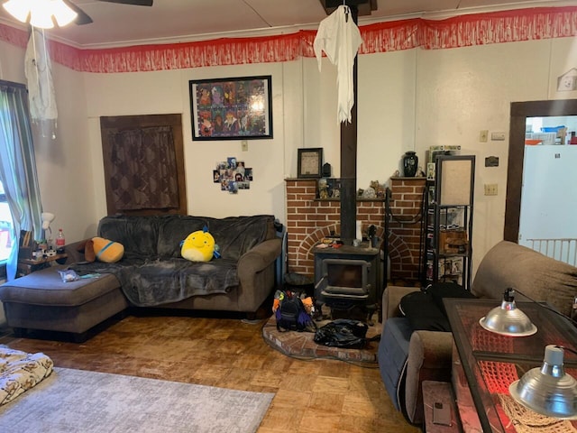 living room with ceiling fan, a wood stove, and ornamental molding