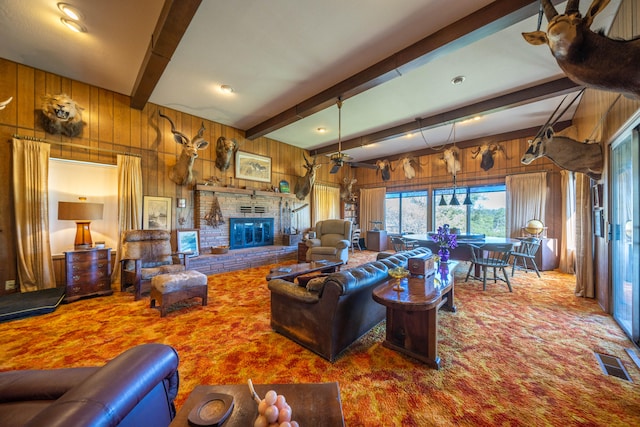 carpeted living room featuring beamed ceiling, ceiling fan, a brick fireplace, and wooden walls