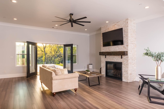 living room featuring crown molding, dark hardwood / wood-style flooring, ceiling fan, and a stone fireplace