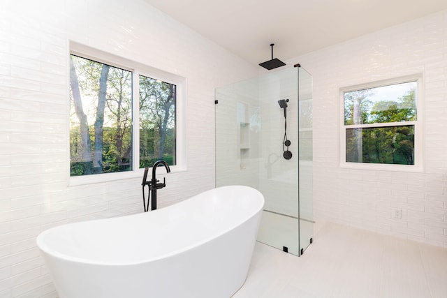 bathroom with a healthy amount of sunlight, a bath to relax in, tile floors, and tile walls