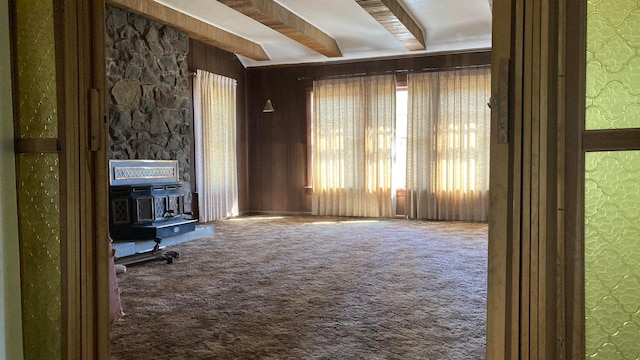 unfurnished living room featuring a wood stove, beamed ceiling, and carpet