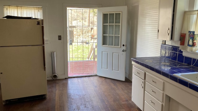 kitchen with white refrigerator, tile countertops, dark hardwood / wood-style flooring, and white cabinets