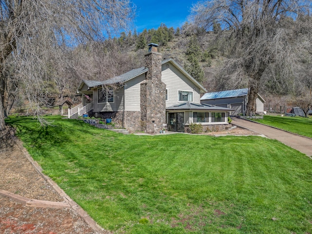 back of property featuring driveway, a lawn, a chimney, and a sunroom