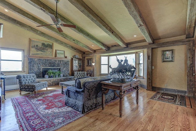 living room featuring a stone fireplace, vaulted ceiling with beams, a ceiling fan, and light wood finished floors