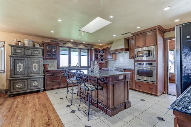 kitchen with a kitchen island, a breakfast bar, custom exhaust hood, a skylight, and stainless steel appliances