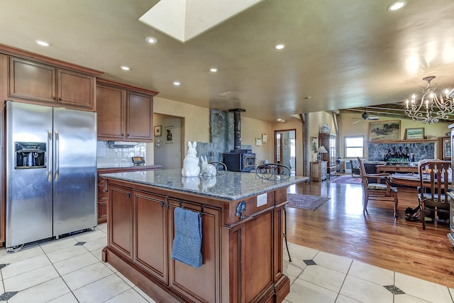 kitchen with a kitchen island, open floor plan, dark stone counters, stainless steel fridge, and light tile patterned floors