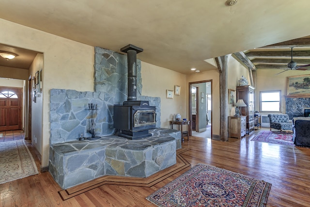 living room with baseboards, a ceiling fan, wood finished floors, and a wood stove