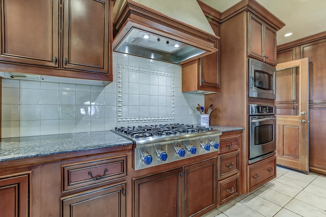 kitchen with dark stone countertops, light tile patterned floors, custom exhaust hood, appliances with stainless steel finishes, and tasteful backsplash