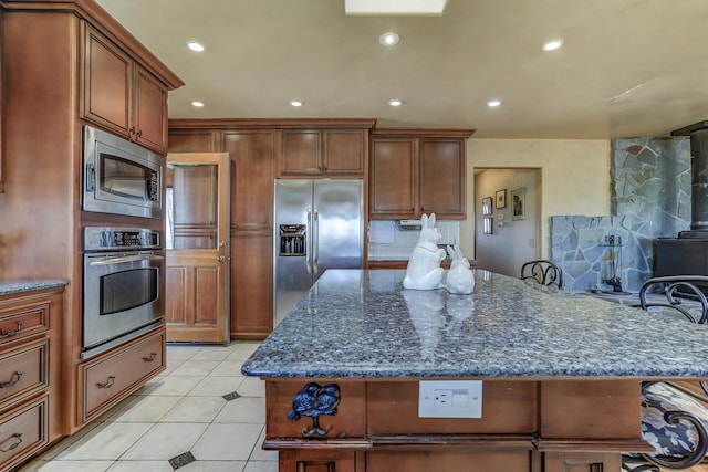 kitchen with dark stone countertops, appliances with stainless steel finishes, light tile patterned flooring, decorative backsplash, and a wood stove