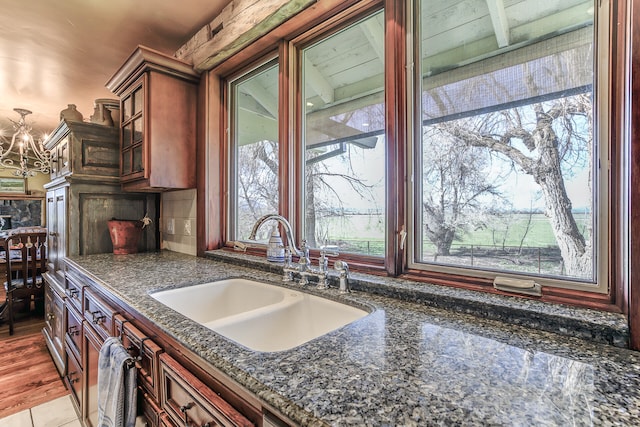 kitchen with a sink, decorative light fixtures, dark stone counters, glass insert cabinets, and a chandelier