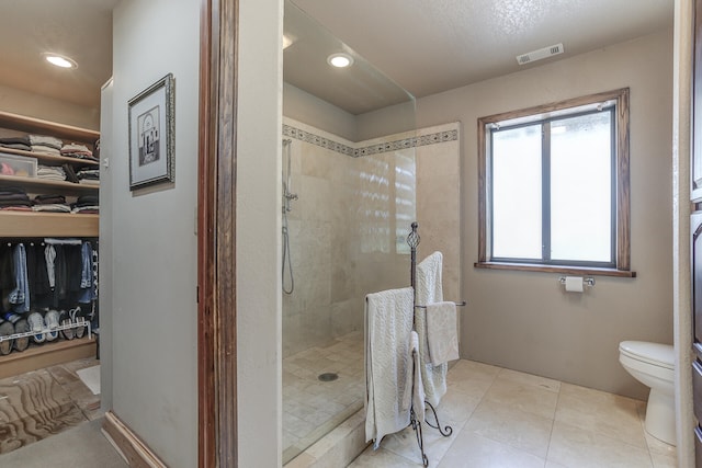 bathroom with visible vents, a walk in closet, toilet, a tile shower, and tile patterned flooring