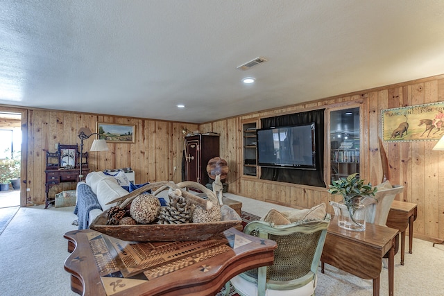 living room featuring visible vents, light colored carpet, a textured ceiling, and wooden walls