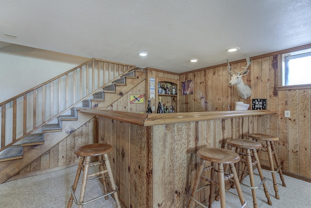 bar with a textured ceiling, stairway, carpet floors, wood walls, and indoor wet bar